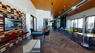 This dynamic single-floor clubhouse is designed to foster community and productivity through a thoughtfully curated open-plan layout. The centerpiece of the space is a sweeping main hall with striking herringbone hardwood flooring and a warm wood-paneled ceiling, creating an inviting contrast against crisp white walls. Soaring ceiling heights amplify the sense of openness, while exposed ductwork adds an industrial edge.

Bold, colorful mosaic tile wall art serves as a recurring design motif, energizing the space with vivid personality. The lounge area features an eclectic mix of seating — including gray sofas, yellow ottomans, and deep red armchairs — arranged around a wall of floor-to-ceiling glass doors that open to views of an outdoor pool courtyard, flooding the interior with natural light.

A dedicated conference room accommodates a full-size boardroom table with yellow upholstered chairs, anchored by a multicolored feature wall and an elegant globe pendant light fixture. The wet bar area is finished in vibrant teal cabinetry with a geometric-patterned backsplash, a stainless steel sink, and open shelving.

A cozy windowed nook with built-in bench seating, striped accent walls, and a sunny yellow table provides an intimate gathering spot. Throughout, curated abstract artwork and a shuffleboard table complete this lively, amenity-rich communal environment.
