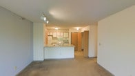 This single-floor unit offers a functional and comfortable layout designed to maximize everyday living. The main living area is generously sized, featuring soft wall-to-wall carpeting underfoot and light-toned walls that lend a clean, airy feel. A large sliding glass door floods the room with natural light and opens to a private balcony, creating an easy indoor-outdoor connection. A wall-mounted air conditioning unit and baseboard heating ensure year-round climate control, while track lighting adds a practical touch.

The kitchen is positioned in an open-concept arrangement, seamlessly connected to the living space via a peninsula breakfast bar — ideal for casual dining or entertaining. It is equipped with essential appliances including a refrigerator, electric range, and built-in microwave, complemented by ample upper cabinetry in a warm wood tone. A hallway leads from the kitchen area toward additional rooms, with a spacious storage or linen closet conveniently accessible nearby. The textured ceilings carry throughout the unit, adding a consistent design element across the space. Overall, the unit presents a straightforward and practical living environment with well-considered features for comfortable day-to-day use.