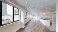 This single-floor space showcases a sleek, contemporary design that emphasizes openness, light, and clean lines. The expansive open-plan layout stretches generously, creating an airy and unobstructed flow throughout the interior. Wide-plank hardwood flooring in warm tones runs the full length of the space, grounding the otherwise crisp, all-white aesthetic with a touch of natural warmth.

A striking row of large, black-framed windows lines one wall, inviting abundant natural light to pour in throughout the day while offering views of the surrounding urban environment. The bright white walls and white ceilings, fitted with recessed lighting, further amplify this sense of brightness and openness.

At one end of the space, a kitchen area is visible, featuring white cabinetry, a marble-patterned backsplash, dark countertops, and elegant pendant lighting that adds a refined finishing touch. The kitchen design is both functional and visually cohesive with the overall modern aesthetic.

The combination of industrial-inspired black window frames, warm hardwood floors, and minimalist white finishes gives the space a sophisticated loft-like character. Whether used as a residential or commercial setting, this thoughtfully designed space offers a versatile, light-filled environment with strong architectural appeal.