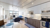 This well-appointed one-bedroom, one-bathroom unit offers a thoughtfully designed open-concept layout that maximizes every square foot. Light wood flooring flows throughout, unifying the living, dining, and kitchen areas into a cohesive, bright space.

The kitchen is a functional highlight, featuring stainless steel appliances — including a refrigerator, electric range, dishwasher, and microwave — paired with two-tone cabinetry: crisp white upper cabinets and wood-grain lower cabinets. Under-cabinet lighting and light countertops complete the clean, modern aesthetic. A compact dining area sits adjacent, ideal for casual meals.

The open living room benefits from expansive windows that frame urban city views and flood the space with natural light. Industrial-style track lighting on exposed ceiling beams adds a contemporary loft-like character to the common areas.

The bedroom is a serene retreat, featuring wide windows with city views, light wood flooring, a sliding closet, and ample room for a full-sized bed and dresser. The bathroom is finished with a floating wood-grain vanity, a white undermount sink, large-format tile flooring, and modern wall-mounted light fixtures flanking a wall mirror — all contributing to a clean, spa-like feel.