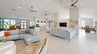 Located at 5001 Willowgate Loop in Fort Myers, Florida, this single-story clubhouse for Tailor offers a generously proportioned, thoughtfully designed community space with a vibrant coastal aesthetic. The reception area greets visitors with a bold tropical-print accent wall, a richly textured reception desk, and plush seating, setting a welcoming and upscale tone throughout.

The expansive main lounge features large-format porcelain tile flooring, soaring ceilings with sleek ceiling fans, and an abundance of recessed lighting. Comfortable sectional sofas, curated artwork, and decorative wall accents create an inviting social atmosphere. Double glass doors open directly to the outdoor pool area, flooding the interior with natural light and offering seamless indoor-outdoor connectivity.

A fully equipped kitchen and bar area anchors the gathering space, complete with granite countertops, stainless steel appliances, built-in cabinetry, a wall-mounted television, and a large island with bar-height seating. An adjacent dining area accommodates multiple seating arrangements beneath vaulted ceilings framed by floor-to-ceiling windows with palm tree views.

Quieter nooks throughout the space provide intimate seating areas adorned with curated artwork, ideal for private conversation or relaxation. The overall design balances a bright, airy Florida coastal palette with bold, contemporary furnishings, making this clubhouse a versatile and visually engaging community hub.