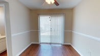 Located at 6000 Mabeline Rd in Hanahan, South Carolina, this two-floor residence offers a straightforward and functional layout with consistent finishes throughout. The main living area features warm hardwood-style flooring that extends across the room, complemented by neutral beige walls with a classic chair rail detail. A ceiling fan provides overhead comfort, while a full-width sliding glass door fitted with vertical blinds allows natural light to filter in and offers access to the outdoors. The open feel of the living space makes it well-suited for flexible furniture arrangements. The kitchen is equipped with white cabinetry that provides ample storage both above and below the countertops. Appliances include a coil-burner electric range, a dishwasher, a full-size top-freezer refrigerator, and an under-cabinet range hood. A double-basin sink sits beneath a window, adding natural light to the workspace. The kitchen also features hardwood-style flooring and a textured ceiling. Additional space is spread across two floors, offering room for separate living and sleeping areas. Overall, the residence presents a clean, well-maintained environment with practical features suited for comfortable everyday living in the Hanahan, SC area.