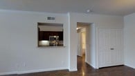 This single-floor residence offers a thoughtfully designed open-concept layout that maximizes the sense of space and flow. The living area features rich, dark hardwood flooring that extends throughout, adding warmth and sophistication to the interior. Crown molding along the ceilings lends a refined architectural touch to the clean, white walls.

The kitchen is designed with both style and function in mind, accessible via a convenient pass-through window that connects it seamlessly to the main living area. Dark espresso cabinetry provides ample storage and creates a striking contrast against the granite countertops. Stainless steel appliances, including a built-in microwave and range, complete the modern kitchen aesthetic.

A hallway visible from the main living space leads to additional rooms, suggesting a well-organized floor plan that balances open communal areas with private spaces. Panel-style doors add a classic touch to the interior design. Recessed HVAC vents are integrated discreetly into the ceiling, maintaining the clean lines of the space. Overall, this residence combines practical functionality with contemporary finishes, creating an inviting and polished living environment.