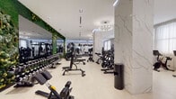 Located at 1401 Spruce Street in Philadelphia's vibrant Center City, this upscale fitness facility delivers a thoroughly equipped and thoughtfully designed workout environment across a single expansive floor. The space is defined by its refined aesthetic, featuring striking white marble-veined columns and accent walls that contrast beautifully with lush green living plant walls and large floor-to-ceiling mirrors that amplify the sense of openness throughout.

The main training floor is generously proportioned, finished with light hardwood-style flooring and illuminated by elegant circular chandelier fixtures and recessed lighting. A comprehensive selection of strength machines, free weights, and cable systems lines the space, complemented by a dedicated functional training zone outfitted with an Octagon rig, suspension trainers, kettlebells, and medicine balls atop durable carpet flooring.

A separate cardio zone features rows of treadmills, ellipticals, and stationary bikes positioned in front of sheer-draped windows that invite soft, natural light into the room. A glass-partitioned studio area houses Pilates reformers, cycling bikes, and additional equipment, offering a more intimate and focused training environment. A further private area with dark wood panel walls accommodates specialty cardio and strength machines. Together, these zones create a cohesive, full-service fitness destination suited to diverse training needs.
