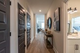This well-appointed single-floor residence offers a thoughtfully designed open-concept layout that seamlessly connects the key living areas. The entryway greets visitors with a welcoming hallway accented by dark-paneled doors with matte black hardware, light wood-look flooring, and decorative wall art — setting an immediately polished tone.

The kitchen is a standout feature, showcasing two-tone cabinetry with white upper cabinets and slate-blue lower cabinets, both fitted with gold hardware. Granite countertops, subway tile backsplash, stainless steel appliances, and a central island complete this functional and stylish space.

The living room is bright and comfortable, featuring large windows that invite natural light, a ceiling fan, and ample room for relaxed seating arrangements. The neutral color palette creates a calm, cohesive ambiance throughout.

The primary bedroom is generously sized with natural light from large windows, a ceiling fan, and direct access to a spacious en suite bathroom. The primary bath includes a dual-sink vanity with granite countertops, black fixtures, and a soaking tub. A second bedroom and additional full bathroom with built-in shelving provide practical accommodations for guests or flexible use. Light wood-look flooring runs consistently throughout, unifying the entire residence.