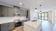 This thoughtfully designed one-bedroom, one-bathroom residence at 531 Laketower Drive in Lexington, KY offers a clean, modern aesthetic throughout its well-appointed single floor. The open-concept kitchen and living area serves as the heart of the home, showcasing gray shaker-style cabinetry, a white subway tile backsplash, stainless steel appliances, and a large center island with a white quartz countertop, undermount sink, and matte black faucet. Stylish globe pendant lights illuminate the island, while recessed lighting brightens the entire space. Warm-toned hardwood-style flooring flows through the main living areas, complementing the neutral color palette. The living area features built-in shelving and access to a private balcony through sleek black-framed sliding glass doors, flooding the space with natural light and outdoor views. The carpeted bedroom is generously sized, with large black-framed windows offering additional natural light and neighborhood views, plus a ceiling fan for comfort. It connects directly to the full bathroom and a walk-in closet outfitted with wire shelving. The bathroom features large-format tile flooring, a white dual-sink vanity with quartz countertops, a wide mirror, and a glass-enclosed shower, delivering a clean, spa-like finish throughout.