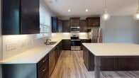 Located in Morrisville, NC, this two-story home offers a well-appointed layout across both levels. The kitchen serves as a central highlight, showcasing dark espresso cabinetry paired with crisp white quartz countertops, a classic subway tile backsplash, and a full suite of stainless steel appliances including a refrigerator, range, microwave, and dishwasher. A large center island with pendant lighting above provides additional workspace and a natural gathering point. Light wood-look flooring runs throughout the main living areas, complementing the neutral gray wall tones and lending a clean, contemporary feel.

The dining area features a chandelier overhead and open sightlines, creating an inviting atmosphere. A convenient half bath on the main level includes a pedestal sink and wood-look flooring. Upstairs, the primary bedroom is generously sized with a tray ceiling, ceiling fan, and windows that allow natural light to filter in. The en-suite bathroom is equipped with a double-sink vanity, a glass-enclosed walk-in shower, and light tile flooring. Additional bedrooms are carpeted and feature windows with views of surrounding greenery. The home's overall design balances modern finishes with comfortable, functional living spaces.