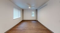 Located at 201 NE 103rd St in Seattle's Northgate neighborhood, this single-floor, 2-bedroom, 1-bathroom residence offers a clean, modern design with a practical and efficient layout. Warm wood-look flooring runs consistently throughout the space, complementing the crisp white walls and light wood trim details found across every room.

The combined kitchen and living area serves as the heart of the home. The kitchen is well-appointed with light maple cabinetry offering generous storage, white appliances including a refrigerator, dishwasher, and electric range, white countertops, and recessed lighting overhead. A window brings in natural light and provides an outdoor view, brightening the space.

Both bedrooms are comfortably sized, each featuring large windows with vertical blinds that allow for natural light and outdoor views. The primary bedroom is notably spacious and includes a wall-mounted HVAC unit for individual climate control. Exposed concrete accent columns add an industrial design touch to both bedrooms.

The bathroom features a light wood vanity with a wide mirror, white countertop, and wood-framed doorways that echo the warm tones found throughout the unit. A dedicated hallway connects all rooms efficiently, and three closets provide ample storage. The entrance corridor, finished with recessed lighting and clean walls, offers a welcoming transition into the home.