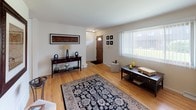 Located at 6411 W Bradley Rd in Milwaukee, Wisconsin, this three-floor property offers a well-organized layout across its levels. The main living area welcomes visitors through a front entry door flanked by a large window fitted with vertical blinds, allowing natural light to brighten the space. Hardwood flooring flows throughout the main level, complementing the open connection between the living and dining areas. The dining space accommodates a table and chairs near another windowed wall, creating a pleasant setting for meals.

The kitchen is equipped with warm-toned wood cabinetry offering generous storage, white appliances including a gas range and dishwasher, a double-basin sink, and light tile flooring. A half bathroom on this level features tile flooring and a pedestal sink. The upper level hosts a bedroom with a window providing natural light, along with a full bathroom featuring a wood-vanity cabinet and wide mirror. An additional room on the upper level includes hardwood floors, a window, and built-in shelving alongside closet space.

The basement spans two distinct areas: a dedicated utility section housing the furnace, water heater, and electrical panel, and a separate open room with painted concrete floors and block walls, well-suited for storage or future finishing.
