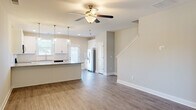 Located at 34 Dolcetto Dr in Winder, Georgia, this two-story home offers three bedrooms and three bathrooms across a well-designed layout. The main floor features an open-concept living and kitchen area finished with durable wood-look flooring and neutral tones throughout. The kitchen is outfitted with crisp white shaker cabinetry, granite countertops, a stainless steel refrigerator, dishwasher, and a breakfast bar with pendant lighting overhead — all illuminated by natural light from multiple windows. A ceiling fan in the living area adds comfort, while a staircase connects seamlessly to the upper level. The upper floor houses all three bedrooms, each carpeted and equipped with ceiling fans. The generously sized primary bedroom includes a walk-in closet with wire shelving. The secondary bedrooms feature windows with outdoor views, providing ample natural light. Three bathrooms serve the home, including one with a full tub-shower combination, white vanity, and wood-look flooring. A dedicated hallway and closet add to the home's functional storage. The overall aesthetic is clean, modern, and move-in ready.