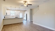 Located at 34 Dolcetto Dr in Winder, Georgia, this two-story home offers three bedrooms and three bathrooms across a well-designed layout. The main floor features an open-concept living and kitchen area finished with durable wood-look flooring and neutral tones throughout. The kitchen is outfitted with crisp white shaker cabinetry, granite countertops, a stainless steel refrigerator, dishwasher, and a breakfast bar with pendant lighting overhead — all illuminated by natural light from multiple windows. A ceiling fan in the living area adds comfort, while a staircase connects seamlessly to the upper level. The upper floor houses all three bedrooms, each carpeted and equipped with ceiling fans. The generously sized primary bedroom includes a walk-in closet with wire shelving. The secondary bedrooms feature windows with outdoor views, providing ample natural light. Three bathrooms serve the home, including one with a full tub-shower combination, white vanity, and wood-look flooring. A dedicated hallway and closet add to the home's functional storage. The overall aesthetic is clean, modern, and move-in ready.