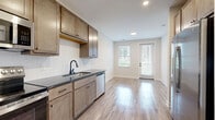 Located at 80 S. Sounders Ave in Columbus, OH, this one-bedroom, one-bathroom unit is thoughtfully designed to maximize its compact footprint across a single floor. The open-concept layout seamlessly combines the kitchen, dining, and living areas into one cohesive, light-filled space. Light wood-look flooring flows throughout the main living areas, complemented by neutral-toned walls that enhance the bright, airy feel. The kitchen is well-equipped with warm-toned shaker-style cabinetry, dark granite countertops, a white subway tile backsplash, and a full suite of stainless steel appliances including a refrigerator, range, microwave, and dishwasher. A door from the living area provides direct access to a private patio. The bedroom features plush carpeting and dual windows that invite natural light and outdoor views. A dedicated closet with built-in wire shelving offers organized storage. The bathroom is finished with a wood-tone vanity, granite countertop, matte black fixtures, and a large mirror. A laundry area and in-unit storage round out this efficiently designed and modern living space.