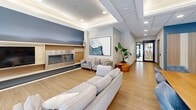 Located at 1425 Block Line Rd in Kitchener, Ontario, this thoughtfully designed amenity space offers a welcoming, open-concept layout spread across a single floor. Light wood-look flooring flows continuously throughout, complementing a neutral palette of whites, warm beiges, and cool blue-grey accent walls that lend the space a calm, modern character.

The lounge area serves as the heart of the space, anchored by a sleek linear gas fireplace set into a warm wood-panelled feature wall. Comfortable grey sofas and lounge chairs are arranged to encourage relaxed gathering, while recessed tray ceilings with integrated lighting add architectural depth overhead. A dedicated TV nook with built-in shelving and large windows overlooking the outdoors provides an additional seating retreat.

The fully equipped kitchen is a standout feature, showcasing stainless steel appliances — including a full-size refrigerator, electric range, and dishwasher — paired with light wood cabinetry, open floating shelves, and a striking blue penny-tile backsplash. A generous island with a crisp white quartz countertop and bar seating makes it ideal for social cooking and entertaining. Pendant lighting above the island adds a refined finishing touch.

A dining area with a large table and upholstered chairs sits adjacent, creating a seamless flow between cooking, dining, and lounging. The space is well-lit through a combination of large windows and recessed ceiling fixtures, fostering an airy, inviting ambiance throughout.