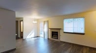 This two-floor space presents a clean, well-maintained interior with a practical and welcoming layout. The main living area is a standout feature, showcasing dark hardwood-style flooring that contrasts elegantly with the light-toned walls, creating a warm yet modern aesthetic. A tile-surround fireplace with a wood mantel serves as the room's focal point, adding both character and functional warmth to the space.

Natural light fills the living area through multiple windows, including a large window overlooking a fenced outdoor area, and a sliding glass door that provides direct access to the exterior. The combination of these openings ensures the room feels open and airy throughout the day. A classic pendant chandelier adds a refined touch to the overall ambiance.

The layout connects seamlessly to adjacent areas, with a hallway visible from the main living space suggesting a thoughtful floor plan that balances openness with defined zones. The two-floor design offers additional living or sleeping areas above, providing ample space for a variety of uses. Overall, the space exudes a tidy, move-in-ready quality with timeless finishes throughout.