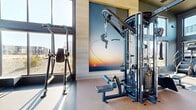 Located at Twin Lakes Ave in Bozeman, Montana, this expansive amenity complex offers a comprehensive wellness and recreation experience across a generously sized single floor. The welcoming lobby sets a sophisticated tone with large-format tile flooring, a stylish lounge area featuring warm wood furnishings, a dramatic black marble accent wall with an integrated TV, and a sleek wet bar with mosaic tile backsplash, dark cabinetry, and open shelving — ideal for community gatherings.

The main fitness center is an impressive, light-filled space defined by soaring double-height ceilings, extensive floor-to-ceiling windows, and a warm wood ceiling detail. Rows of commercial-grade treadmills, ellipticals, and stair climbers line the perimeter, while a robust selection of Matrix strength machines, cable systems, and free weights fill the floor. Large wall-mounted TVs and motivational artwork enhance the energetic atmosphere.

A dedicated yoga and spin studio features light hardwood flooring, large windows framing Montana mountain views, spin bikes, yoga mats, and ceiling fans — creating a bright, calming environment. The sports simulator room offers an immersive Full Swing system for golf and multi-sport gaming. Together, these spaces form a well-appointed, amenity-rich destination designed to support an active lifestyle.