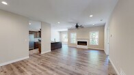 This single-story home in Boonville, Missouri presents a thoughtfully designed open-concept floor plan that seamlessly connects the main living areas. Light-toned hardwood flooring runs throughout the primary living spaces, contributing to a clean, cohesive aesthetic that enhances the sense of openness.

The living area serves as a central focal point, anchored by a sleek, wall-mounted electric fireplace set within a white shiplap surround and mantel. Multiple double-hung windows flank the fireplace, allowing natural light to fill the space while framing views of the surrounding greenery. A ceiling fan with a stylish fixture complements the recessed lighting overhead.

The kitchen is well-appointed with rich dark cabinetry, granite countertops, stainless steel appliances including an electric range, microwave, refrigerator, and dishwasher, and a large island with a built-in sink. The layout allows for a smooth flow into the dining and living areas.

Bedrooms are finished with plush carpet and ceiling fans, offering a comfortable retreat. One bedroom features a tray ceiling detail and direct exterior access. The bathroom includes a walk-in shower, vanity with a white countertop, and coordinating hardwood-style flooring, maintaining consistency with the home's overall design language.