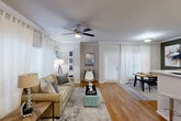 Located in Spring, TX, this well-appointed 3-bedroom, 2-bathroom single-floor residence offers a thoughtfully designed layout with cohesive finishes throughout. The living room features warm wood-look flooring, crown molding, a ceiling fan with light fixture, and large windows dressed in sheer white curtains that flood the space with natural light. Adjacent to the living area, the dining room provides an intimate setting with a natural wood dining table, bold accent wall, and direct access to an exterior door. The galley-style kitchen is efficiently organized with rich wood cabinetry, stainless steel appliances, a double sink, tile backsplash, and matching wood-look flooring. The primary bedroom is a comfortable retreat with plush carpeting, a ceiling fan, built-in desk area, and ample natural light. The two bathrooms are each equipped with a full tub-shower combination featuring classic white tile with a decorative gold accent stripe and wood-look flooring. A carpeted hallway connects the bedrooms to the bathrooms, with closet access conveniently located nearby. Crown molding and neutral tones are carried consistently throughout, lending a clean, unified aesthetic to the entire home.