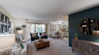 This single-floor residence offers a well-organized layout that balances open communal spaces with comfortable private areas. The living room serves as the heart of the home, featuring plush carpeting, a ceiling fan, and large sliding windows that frame views of mature trees, filling the space with natural light. A boldly painted teal accent wall adds a striking focal point, complemented by neutral tones throughout the rest of the room. The living and dining areas flow seamlessly together, creating an open, airy feel ideal for everyday living and entertaining.

The kitchen is equipped with warm honey-toned wood cabinetry, dark laminate countertops, and white appliances including a gas range, dishwasher, and refrigerator. A peninsula with pendant lighting provides additional prep space and a casual dining option. Tile flooring runs throughout the kitchen for easy maintenance.

The primary bedroom features hardwood-style flooring, soft sage-green walls, and a walk-in closet with built-in shelving. A second bedroom offers ample space with hardwood-style floors. Both bathrooms are finished with tile flooring and white fixtures, with one featuring an extended vanity and a large mirror. The overall ambiance throughout is warm, cozy, and thoughtfully styled.