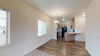 This 1-bedroom unit offers a thoughtfully laid-out, single-floor living space that seamlessly blends comfort and functionality. The open-concept design connects the living area and kitchen, creating a cohesive and airy environment. Smooth, neutral-toned walls and a clean white ceiling provide a bright, welcoming atmosphere throughout.

The living area features warm wood-look hard flooring that transitions into plush carpeting, adding texture and comfort underfoot. A window fitted with horizontal blinds allows natural light to filter in, enhancing the overall sense of openness.

The kitchen is a standout feature, appointed with light wood cabinetry that offers ample storage space. Black appliances, including a full-size refrigerator and dishwasher, provide a modern contrast against the lighter cabinetry. A breakfast bar with a smooth countertop extends from the kitchen, offering a casual dining or workspace option. An elegant chandelier overhead adds a refined touch, illuminating both the kitchen and the adjacent dining space.

The cohesive design choices throughout — from the consistent flooring to the neutral color palette — give this unit a clean, move-in-ready appeal that is both practical and visually inviting.