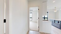 This thoughtfully designed 2-bedroom, 2-bathroom residence offers a bright, contemporary living experience across a single floor. The open-concept kitchen serves as the heart of the home, showcasing white shaker cabinetry with gold hardware, a crisp quartz countertop, and a striking two-tone center island in slate blue with a built-in microwave. Stainless steel appliances — including a gas range with a stainless hood, refrigerator, and dishwasher — are complemented by a white subway tile backsplash and a gold-finished faucet. Globe pendant lights with brass accents add a refined touch overhead. Light wood-look flooring flows throughout the main living areas, while large black-framed windows invite abundant natural light into the open living space, which also features access to a private balcony. Both bedrooms are carpeted and include ceiling fans and oversized black-framed windows with outdoor views. The primary bedroom offers a generous footprint with its own closet. The bathrooms are finished with white cabinetry, quartz countertops, black hardware accents, and wood-look tile flooring. Two closets and a dedicated hallway round out this well-appointed, modern residence.