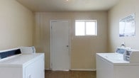 This single-floor space presents a practical and straightforward layout centered around a dedicated laundry room. The laundry area is equipped with both a washer and dryer, positioned on either side of the room for convenient use. The space features neutral beige walls that create a clean, understated aesthetic, complemented by tile flooring that is durable and easy to maintain. A single window allows natural light to filter into the room, brightening the otherwise utilitarian space. A white interior door provides access to an adjoining area, adding to the overall flow of the layout. The room is designed with functionality in mind, offering ample space around the appliances for ease of movement. Baseboard trim lines the perimeter of the room, adding a subtle finishing detail to the walls. The overall ambiance is practical and no-frills, making this space well-suited for efficient everyday use. The simple, clean design ensures the laundry area remains organized and easy to navigate.