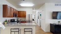 This single-floor residence offers a thoughtfully designed layout that balances functionality and comfort throughout. The open-concept kitchen serves as the heart of the home, showcasing warm honey-toned cabinetry, granite countertops, and a full suite of stainless steel appliances including a gas range, over-the-range microwave, and a side-by-side refrigerator. A peninsula with bar seating provides an ideal casual dining spot while maintaining a seamless connection to the living area. Light hardwood-style flooring runs through the main living spaces, enhancing the bright, airy atmosphere created by large windows dressed with grommet-top curtains. The living room is welcoming and spacious, featuring a ceiling fan and access to an exterior door, allowing natural light to fill the space. Bedrooms offer plush carpeting, double-door closets, and windows that bring in additional natural light. The bathroom is well-equipped with a generous granite vanity, rich wood cabinetry, a wide mirror, and a tub-shower combination. A dedicated in-unit laundry room with a full-size washer and dryer adds everyday convenience. Throughout, the neutral color palette and clean finishes create a cohesive, move-in-ready environment.