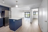 Located at 3385 Dundas St W in Toronto's Junction neighbourhood, this one-bedroom, one-bathroom unit offers a well-designed layout with modern finishes throughout. Light wood laminate flooring runs continuously across the entire space, contributing to a clean, cohesive aesthetic.

The open-concept kitchen and living area serves as the heart of the unit. The kitchen is outfitted with striking blue cabinetry, a white subway tile backsplash, stainless steel appliances including a fridge, gas range, and microwave, and a central island with a white countertop that doubles as a breakfast bar. A pendant light fixture overhead adds a refined touch. Large floor-to-ceiling windows with black frames flood the living area with natural light and provide views of the surrounding Dundas Street West streetscape.

The bedroom is a comfortable, well-proportioned room featuring a window with an exterior view and direct access to a dedicated closet, offering practical storage. The clean white walls and light flooring create a calm, restful environment.

The bathroom is finished with neutral tile flooring, white wall tiles, and a full soaker tub and shower combination. The overall design of the unit prioritizes clean lines, functional use of space, and a bright, contemporary atmosphere throughout.