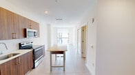 Located in Miami's vibrant urban core, this single-floor residence at 218 NW Eighth St offers a clean, contemporary design throughout. Large-format porcelain tile flooring runs continuously across the space, lending a cohesive and polished look to every room.

The kitchen is a standout feature, outfitted with warm walnut-toned cabinetry accented by gold hardware, a full suite of stainless steel appliances including a refrigerator with ice maker, electric range, built-in microwave, and dishwasher. A white subway tile backsplash adds texture, while a freestanding island with a light wood top provides additional prep and dining space.

The open living and dining area extends toward floor-to-ceiling windows that flood the interior with abundant natural light and frame dynamic views of the Miami skyline and surrounding cityscape. A ceiling fan with a wood-accented fixture adds a practical touch to the bright, airy bedroom, which also benefits from expansive window views.

The bathroom is finished with marble-look tile in the tub and shower surround, complemented by walnut cabinetry with gold hardware and a clean white countertop. A generously sized closet with double doors and a full-width hanging rod provides ample storage. Recessed lighting throughout keeps the interiors bright and modern.