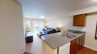 Located at 6950 Birdseye Ave NE in Olympia, WA, this single-floor apartment offers a thoughtfully designed layout with a warm, neutral color palette throughout. The open-concept kitchen flows seamlessly into the living area, making it ideal for everyday living and entertaining. The kitchen features rich warm-toned cabinetry, a spacious gray countertop peninsula with a built-in sink, a full suite of white appliances including a refrigerator, range, microwave, and dishwasher, and durable wood-style flooring. The living area is bright and welcoming, with plush carpeting and sliding glass doors that open to a private balcony with outdoor views. The primary bedroom is generously sized with carpet flooring, a large window that invites natural light, and ample wall space. A secondary bedroom offers similar comfort and natural light. A flexible den or office space features a large window overlooking greenery, providing a calm and productive environment. The full bathroom includes a soaking tub and shower combination, while a second half-bath features a wood-cabinet vanity and wood-style flooring. Together, these spaces create a functional and comfortable living environment suited to a variety of lifestyles.