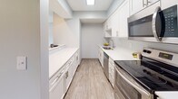 This single-floor residence offers a clean, modern aesthetic throughout, with neutral gray walls, white trim, and textured ceilings that lend a cohesive and welcoming feel. The open living area is finished with wood-look luxury vinyl flooring and features a sliding glass door fitted with vertical blinds, inviting natural light and providing direct access to an outdoor area with views of surrounding greenery. An adjacent space flows seamlessly from the living area, extending the sense of openness and flexibility.

The galley-style kitchen is thoughtfully designed with crisp white cabinetry, white quartz countertops, a skylight, and stainless steel appliances including a range, dishwasher, and microwave. A pass-through counter connects the kitchen to the living space, enhancing both functionality and flow.

Multiple bedrooms feature plush wall-to-wall carpeting and large windows dressed with horizontal blinds, filling each room with natural light and views of the outdoors. The rooms offer a quiet, comfortable atmosphere well-suited for rest or use as a home office.

Two full bathrooms are appointed with white vanity cabinetry, brushed nickel hardware, white countertops, wood-look vinyl flooring, and tub-shower combinations, presenting a clean and polished finish throughout.