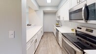 This single-floor residence offers a clean, modern aesthetic throughout, with neutral gray walls, white trim, and textured ceilings that lend a cohesive and welcoming feel. The open living area is finished with wood-look luxury vinyl flooring and features a sliding glass door fitted with vertical blinds, inviting natural light and providing direct access to an outdoor area with views of surrounding greenery. An adjacent space flows seamlessly from the living area, extending the sense of openness and flexibility.

The galley-style kitchen is thoughtfully designed with crisp white cabinetry, white quartz countertops, a skylight, and stainless steel appliances including a range, dishwasher, and microwave. A pass-through counter connects the kitchen to the living space, enhancing both functionality and flow.

Multiple bedrooms feature plush wall-to-wall carpeting and large windows dressed with horizontal blinds, filling each room with natural light and views of the outdoors. The rooms offer a quiet, comfortable atmosphere well-suited for rest or use as a home office.

Two full bathrooms are appointed with white vanity cabinetry, brushed nickel hardware, white countertops, wood-look vinyl flooring, and tub-shower combinations, presenting a clean and polished finish throughout.