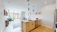 This well-appointed one-bedroom, one-bathroom unit showcases a thoughtfully designed modern interior with a clean, contemporary aesthetic. Light wood flooring runs throughout, complementing the bright, neutral palette of the walls and ceilings.

The open-concept kitchen and living area serves as the heart of the unit. The kitchen features light wood cabinetry with matte black hardware, white quartz countertops, stainless steel appliances including a full-size refrigerator, range, and dishwasher, and a peninsula with bar seating illuminated by sleek pendant lighting. White upper cabinets and a subway tile backsplash add a classic touch.

The living area is anchored by expansive floor-to-ceiling windows that flood the space with natural light and offer open views of the surrounding neighborhood streetscape. The hallway entry features additional wall space well-suited for artwork or décor.

The bedroom is a comfortable and well-lit retreat, benefiting from its own large windows with neighborhood views, and includes access to a dedicated closet. The bathroom mirrors the home's modern design language, featuring a floating vanity with light wood cabinetry, white quartz countertop, an undermount sink with chrome fixtures, and tile flooring. The overall ambiance of the unit is bright, airy, and move-in ready.