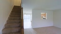 Located at 100 N Barrett Lane in Newark, Delaware, this three-floor home offers a well-organized multi-level layout designed for comfortable everyday living. The main living area features neutral-toned carpeting that extends throughout, contributing to a warm and cohesive atmosphere. A carpeted staircase with a classic wooden banister connects the floors, serving as a central architectural element visible from the main living space.

The living area benefits from an abundance of natural light, courtesy of large vertical-blind-covered sliding doors or windows that face outward, brightening the interior considerably. A pass-through window connects the living space to the kitchen, providing an open sightline that enhances the sense of connectivity between rooms. The kitchen is equipped with light wood cabinetry and standard appliances, offering a practical and efficient workspace.

The layout flows naturally between the living and kitchen areas, making the main floor feel open and approachable. The multi-floor design provides clear separation between living, sleeping, and additional functional spaces across the three levels, accommodating a variety of lifestyle needs throughout the home.