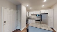 Located at 240 Pine Knot Lane in Graham, North Carolina, this single-floor unit offers a thoughtfully designed layout with modern finishes throughout. The kitchen serves as a functional centerpiece, showcasing white shaker-style cabinetry, granite countertops, and a full suite of stainless steel appliances, including a range with a stainless hood vent, built-in microwave, dishwasher, and refrigerator. A granite-topped island provides additional prep space and casual seating. Recessed lighting and durable wood-look flooring complete the kitchen's clean, contemporary aesthetic.

The living area is generously proportioned, finished with neutral-toned carpet and accented by French doors that invite natural light. A separate bedroom features plush carpeting, a ceiling fan with light fixture, and windows overlooking the exterior. The bathroom includes a tiled tub-shower combination and tile flooring, with convenient built-in shelving for storage. An expansive walk-in closet adjacent to the bedroom offers extensive wire shelving and hanging space along multiple walls. Neutral wall tones and consistent finishes throughout contribute to a cohesive, move-in-ready environment.