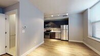 Located at 23 Central in Lynn, Massachusetts, this single-floor unit offers a clean, contemporary design with a thoughtfully arranged open-concept layout. The main living area features light hardwood flooring that extends throughout, creating a warm and cohesive aesthetic. Large windows fitted with blinds flood the space with natural light, enhancing the bright, airy ambiance.

The kitchen is a standout feature, outfitted with dark-toned cabinetry, white countertops, and a full suite of stainless steel appliances including a refrigerator, electric range, microwave, and dishwasher. A subway tile backsplash adds a modern touch, while track lighting overhead ensures excellent task illumination. The kitchen flows seamlessly into the living area, making the space well-suited for everyday living.

The bedroom area is generously sized, benefiting from corner windows on two walls that invite abundant natural light and provide an open, comfortable feel. Hardwood flooring and track lighting continue throughout this room.

The bathroom is finished with neutral tile flooring, a white vanity with under-cabinet storage, a mirror, and a combined tub and shower. The muted gray wall tones create a calm, functional space. A in-unit washer and dryer is also included, as visible in the floor plan layout, adding a practical convenience to this well-appointed unit.
