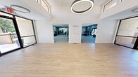 Located at 8401 Spain Rd NE in Albuquerque, New Mexico, this modern fitness center offers a comprehensive workout facility spread across a generously sized single floor. The space is divided into three distinct functional zones, each thoughtfully designed to support a variety of fitness activities.

The main entry area serves as a bright, open studio space featuring light wood-tone flooring, soaring vaulted ceilings, large clerestory windows that flood the room with natural light, and a striking circular overhead pendant light fixture. Glass sliding doors provide direct access to the outdoors, enhancing the sense of openness.

Adjacent to the studio, the cardio room is carpeted and lined with large French doors that overlook the exterior grounds. It houses a full lineup of cardio equipment including treadmills, ellipticals, stationary bikes, and spin cycles, all positioned to take advantage of the natural views.

The strength training area is equally well-appointed, offering a wide selection of free weights, dumbbells, a multi-station cable machine, weight benches, stability balls, resistance bands, and a rowing machine. Floor-to-ceiling mirrors enhance the sense of space and support proper form during workouts.

A smaller auxiliary area provides additional functional training space with mats and accessories. Throughout, the facility maintains a clean, contemporary aesthetic with neutral gray tones, recessed lighting, and durable carpeted flooring in the workout zones.