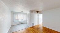 Located at 15111 Greenfield Road in Detroit, MI, this one-bedroom, one-bathroom unit offers a practical and well-organized layout across a single floor. Warm-toned hardwood flooring runs throughout the main living areas and bedroom, lending a classic character to the space. The living room is bright and open, featuring a large window with vertical blinds that allow natural light to fill the room, complemented by a textured ceiling and a wall-unit air conditioner. The kitchen is compact yet functional, equipped with bold teal-blue upper and lower cabinetry, a marble-patterned countertop with an integrated sink, and white appliances including a refrigerator and electric range. The bedroom is a comfortable, well-proportioned space with the same rich hardwood flooring, a closet with louvered doors, and a ceiling-mounted HVAC unit. The bathroom features warm peach-toned tile lining the walls and a mosaic tile floor, with a full shower and tub combination, a window for natural ventilation, and a clean white toilet and sink. A dedicated closet provides additional storage. The unit's clean white walls and consistent flooring throughout create a cohesive, move-in ready feel.