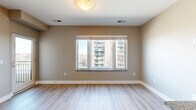 This efficiently designed single-floor unit offers a thoughtful layout that maximizes every square foot. The galley-style kitchen is a standout feature, showcasing rich dark espresso cabinetry, granite countertops, a stainless steel appliance suite including a refrigerator, dishwasher, and range, as well as track lighting overhead and a peninsula that opens toward the main living area. Light hardwood-style flooring extends throughout the space, lending warmth and visual continuity. The open living area benefits from a large multi-pane window that frames views of the surrounding urban landscape, filling the room with natural light. A glass door provides direct access to a private balcony, further enhancing the connection to the outdoors. Ample closet storage is integrated near the entryway, offering practical organization solutions. The bathroom is finished with large-format tile flooring, granite vanity countertop with cabinetry below, and a full soaking tub with tile surround. Neutral warm-toned walls throughout the unit create a calm, cohesive ambiance. The overall design balances modern finishes with functional efficiency, making it a well-equipped and comfortable urban living space.