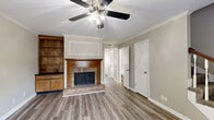 Located at 2160 N Thompson Ln in Murfreesboro, TN, this two-story home offers a thoughtful layout across two floors. The main level provides the most expansive living area, highlighted by a welcoming living room with wood-look luxury vinyl plank flooring, crown molding, a ceiling fan, and a classic brick fireplace with a warm wood mantel. Built-in shelving and cabinetry flank the fireplace, adding both character and storage. Adjacent to the living room, the dining area features crown molding, a chandelier, and chair rail detailing, lending a polished, traditional feel. The galley-style kitchen is lined with warm wood cabinetry on both sides, vaulted ceiling with an exposed beam, and a window above the sink allowing natural light to filter in. A full bathroom on the main level features wood-toned cabinetry and updated fixtures. The carpeted staircase with a classic wood banister and white spindles leads to the upper level, where both bedrooms are situated. Each bedroom is finished with plush carpet, ceiling fans, and closets, with natural light provided by windows. The second full bathroom serves the upper floor. Neutral tones throughout create a clean, move-in-ready atmosphere.