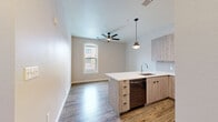Located at 1100 Washington Ave in Golden, Colorado, this thoughtfully designed 2-bedroom, 2-bathroom residence offers a modern aesthetic with high-quality finishes throughout. The open-concept kitchen is a standout feature, showcasing light wood-grain cabinetry, a large quartz island with an undermount sink and bar seating, stainless steel appliances including a full-size range with a stainless hood, a built-in microwave, and a refrigerator. Elegant pendant lighting and tile backsplash complete the contemporary look, while durable wood-style flooring flows seamlessly into the adjoining living area, which features a ceiling fan and natural light from an arched window. Both bathrooms are finished with large-format stone tile flooring, wood-tone vanities with white countertops, and frameless glass walk-in showers with grey subway tile surrounds. The two bedrooms are carpeted for comfort, each benefiting from natural light via windows and generous closet space with panel-style doors. Additional conveniences include in-unit laundry, ample closet storage throughout, and a well-connected hallway layout. The residence presents a clean, neutral palette that lends itself to a variety of interior styles.