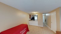 This two-floor residence offers a practical and comfortable layout designed for everyday living. The main level showcases an open-concept design where the living area flows seamlessly into the kitchen. The living space features neutral-toned carpeting and warm beige walls, creating a clean and welcoming atmosphere throughout.

The kitchen is positioned at the heart of the main level, separated from the living area by a half-wall pass-through counter with a light stone-toned surface. The kitchen is equipped with medium-toned wood cabinetry, black appliances, and a window above the sink that allows natural light to filter into the space. The pass-through design enhances the sense of openness while maintaining a defined cooking area.

A textured ceiling runs throughout the main level, adding subtle visual interest overhead. A hallway visible beyond the kitchen leads toward additional spaces, while a staircase on the right side of the main level provides access to the upper floor. The overall ambiance of the home is neutral and understated, offering a versatile canvas well-suited to a range of interior styles and furnishing preferences.