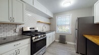 Located at 385 E 222nd St in Euclid, Ohio, this single-floor unit offers a practical and well-maintained living space with a blend of classic architectural details and modern updates. The layout, visible in the floor plan, reveals a series of connected rooms with a logical flow between living areas, bedrooms, and the kitchen.

The kitchen stands out as a highlight of the space, featuring white shaker-style cabinetry, a white subway tile backsplash, a natural wood open shelf, and stainless steel appliances including a gas range and refrigerator. Light gray luxury vinyl plank flooring, a window with outdoor views of surrounding greenery, and a cast-iron radiator complete the room's functional and updated aesthetic.

The living and bedroom areas feature warm-toned hardwood flooring that adds character throughout. Multiple windows allow natural light to filter in, brightening the neutral gray walls. Cast-iron radiators are present in several rooms, underscoring the building's traditional heating system while adding a period-appropriate architectural detail.

The bathroom includes a full-size soaking tub, a white vanity with cabinet storage, a wall-mounted mirror, and multiple windows that provide natural light. Light wood-tone flooring ties the space together with a clean, minimal look throughout.