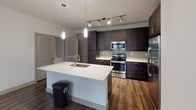 This single-floor residence in Dallas, Texas offers a thoughtfully designed layout with modern finishes and a cohesive aesthetic throughout. The kitchen is a standout feature, showcasing rich dark cabinetry, white quartz countertops, a large center island with an undermount sink, stainless steel appliances — including a French door refrigerator, range, and microwave — plus a classic tile backsplash and track lighting overhead. Pendant lights above the island add a warm, contemporary touch.

The bedrooms are generously proportioned, with plush carpeting, ceiling fans, and windows fitted with blinds that bring in natural light. The primary bedroom connects directly to its en-suite bathroom and a spacious walk-in closet, which features dual hanging rods and built-in shelving for ample storage.

The bathrooms are finished with rich, dark wood-toned vanities, white countertops, large mirrors with vanity lighting, and wood-look flooring that adds warmth. Each bathroom offers a clean, modern feel with well-placed fixtures. An additional room with neutral carpet provides flexible space suitable for a bedroom or office. The overall ambiance is clean and contemporary, with a neutral palette and quality finishes that offer a comfortable, move-in-ready living environment.