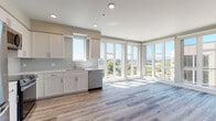 Located at 1235 Oakmead Pkwy in Sunnyvale, California, this single-floor unit presents a clean, contemporary design characterized by light hardwood-style flooring, neutral warm-toned walls, and white trim that run consistently throughout the space. The open-concept kitchen and living area serves as the centerpiece of the unit, where a wall of floor-to-ceiling windows and glass panel doors floods the interior with abundant natural light and offers expansive views of the surrounding Sunnyvale skyline and greenery. The kitchen is outfitted with white shaker-style cabinetry, light quartz countertops, a subway tile backsplash, and a full suite of stainless steel appliances including a refrigerator, range, built-in microwave, and dishwasher. The living area flows generously from the kitchen, benefiting from the same bright, airy atmosphere created by the corner window configuration. Additional rooms feature large windows that bring in natural light and views of the neighboring streetscape. The bathrooms are finished with white cabinetry, quartz countertops, and light wood-tone flooring. One bathroom includes a tub-shower combination, while another features a frameless glass walk-in shower with white subway tile walls and brushed nickel hardware, conveying a polished, modern aesthetic.
