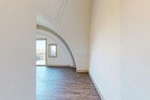 Located at 870 Westminster St in Providence, RI, this two-bedroom, one-bathroom two-story space is a standout example of distinctive architectural character. The structure's defining feature is its dramatic barrel-vaulted arched ceiling, which sweeps gracefully across the upper level and creates a sense of grandeur and volume rarely found in residential spaces. Decorative ornamental molding with a classical Greek key motif adorns one of the arches, adding a refined artistic touch to the interior.

Hardwood-style flooring runs throughout both floors, providing a warm and cohesive aesthetic. The generously sized primary bedroom occupies a significant portion of the upper floor, featuring soaring curved ceilings, prominent arched structural elements, and a sliding glass door that opens directly onto a private balcony with open city views. A charming circular porthole window on the upper level floods the space with natural light.

The lower floor offers additional living space beneath a curved architectural overhang, with pendant lighting and rich, dark-toned flooring. The bathroom is clean and modern, featuring a warm wood-toned vanity, illuminated mirrors, a glass-enclosed shower, and hardwood-style flooring. A dedicated walk-in closet with built-in shelving and rod storage completes the layout. Hallways and a staircase connect the two floors seamlessly throughout this architecturally memorable Providence residence.