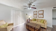 This well-appointed single-floor residence offers a thoughtful layout that maximizes every square foot across one bedroom, one bathroom, and a combined living, dining, and kitchen area. The living room serves as the heart of the home, featuring durable wood-look flooring, a ceiling fan with light fixture, a cozy fireplace, and large sliding glass doors dressed with vertical blinds that invite natural light. The adjacent dining area provides a defined space for meals, complemented by neutral walls and the same wood-look flooring that flows throughout the common areas. The galley-style kitchen is efficiently designed with dark cabinetry, light stone-look countertops, stainless steel appliances including a refrigerator, microwave, and electric range, plus an in-unit washer and dryer tucked neatly at the end of the corridor. The bedroom offers a carpeted floor, a window with curtains for natural light and privacy, a textured ceiling, and a closet for ample storage. The bathroom includes a tiled shower-tub combination, a vanity with a speckled countertop, and wood-look flooring. Throughout the unit, textured ceilings and clean white walls create a bright, cohesive ambiance.