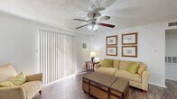 This well-appointed single-floor residence offers a thoughtful layout that maximizes every square foot across one bedroom, one bathroom, and a combined living, dining, and kitchen area. The living room serves as the heart of the home, featuring durable wood-look flooring, a ceiling fan with light fixture, a cozy fireplace, and large sliding glass doors dressed with vertical blinds that invite natural light. The adjacent dining area provides a defined space for meals, complemented by neutral walls and the same wood-look flooring that flows throughout the common areas. The galley-style kitchen is efficiently designed with dark cabinetry, light stone-look countertops, stainless steel appliances including a refrigerator, microwave, and electric range, plus an in-unit washer and dryer tucked neatly at the end of the corridor. The bedroom offers a carpeted floor, a window with curtains for natural light and privacy, a textured ceiling, and a closet for ample storage. The bathroom includes a tiled shower-tub combination, a vanity with a speckled countertop, and wood-look flooring. Throughout the unit, textured ceilings and clean white walls create a bright, cohesive ambiance.