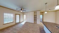 This single-floor residence offers a thoughtfully designed layout that balances open communal spaces with comfortable private areas. The spacious living room serves as the heart of the home, featuring plush wall-to-wall carpeting, crown molding, a ceiling fan with light fixture, and built-in shelving that adds both function and character to the space. A sliding glass door floods the room with natural light and provides exterior access, while an open sightline connects directly to the kitchen. The kitchen is designed in a galley configuration, showcasing rich dark cabinetry, granite-style countertops, black appliances including a refrigerator and electric range, a double stainless steel sink, and warm hardwood-style flooring. Pendant and track lighting illuminate the space efficiently. A breakfast bar with countertop seating bridges the kitchen and living area seamlessly. The bedrooms are generously sized, each with soft carpeting, ceiling fans, and large windows dressed with blinds that invite ample natural light. The bathrooms feature hardwood-style flooring, dark vanity cabinetry with granite-style countertops, and large mirrors. One bathroom includes a tub-shower combination, while the other offers a more streamlined layout. Throughout the residence, neutral tones and consistent finishes create a cohesive, inviting ambiance.