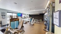 Located at 281 Willow St in Fort Collins, Colorado, this well-appointed fitness center offers a spacious, single-floor open layout designed to accommodate a full range of workout activities. The interior features a clean, modern aesthetic with a neutral color palette, accented by soft yellow walls and a bold textured dark feature wall that adds visual depth to the space.

Overhead, linear pendant lighting and recessed fixtures provide bright, even illumination throughout, complementing the natural light that streams in through large floor-to-ceiling windows. These windows also offer views of the surrounding outdoor areas, creating an open and energizing atmosphere.

The cardio zone is well-equipped with a row of Matrix treadmills, ellipticals, and stair climbers, all positioned to take advantage of the natural light and wall-mounted flat-screen TVs. The strength training area features a multi-station cable machine, a full dumbbell rack, stability balls, benches, and a variety of selectorized machines, providing options for a complete full-body workout.

Durable rubber flooring covers the entire space, offering both safety and comfort underfoot. The layout is thoughtfully organized to maximize circulation and usability, making this fitness center a functional and inviting environment for users of all fitness levels.