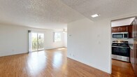 Located in the Granada Hills neighborhood of Los Angeles, this 2-bedroom, 1-bathroom residence offers a well-organized single-floor layout with consistent hardwood flooring throughout. The open-concept living room is bright and airy, featuring a textured ceiling, a ceiling fan, a skylight, and large sliding glass doors that open to a balcony with outdoor views of mature trees—filling the space with natural light. The kitchen is well-appointed with rich wood cabinetry, granite countertops, stainless steel appliances, and ample storage, including tall upper cabinets that maximize vertical space. The primary bedroom is generously proportioned, offering a dedicated walk-in closet with built-in shelving rods on both sides, providing excellent storage capacity. The second bedroom includes a sliding-door closet and continues the hardwood flooring found throughout the home. The bathroom features tile flooring, a wood vanity with a granite countertop, and a shower-tub combination. A hallway connects the bedrooms to the main living areas. The overall ambiance is clean, bright, and functional, with a neutral color palette that lends itself well to a variety of interior styles.